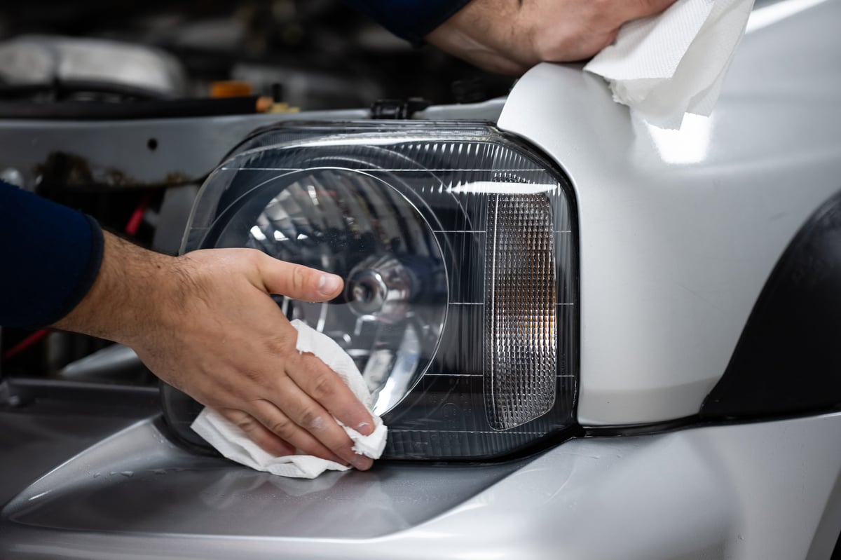 Man's hands cleaning a car headlight with a white cloth